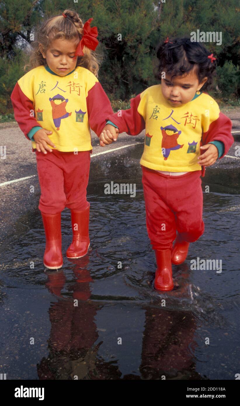 two little sisters in red wellies splashing through puddles Stock Photo