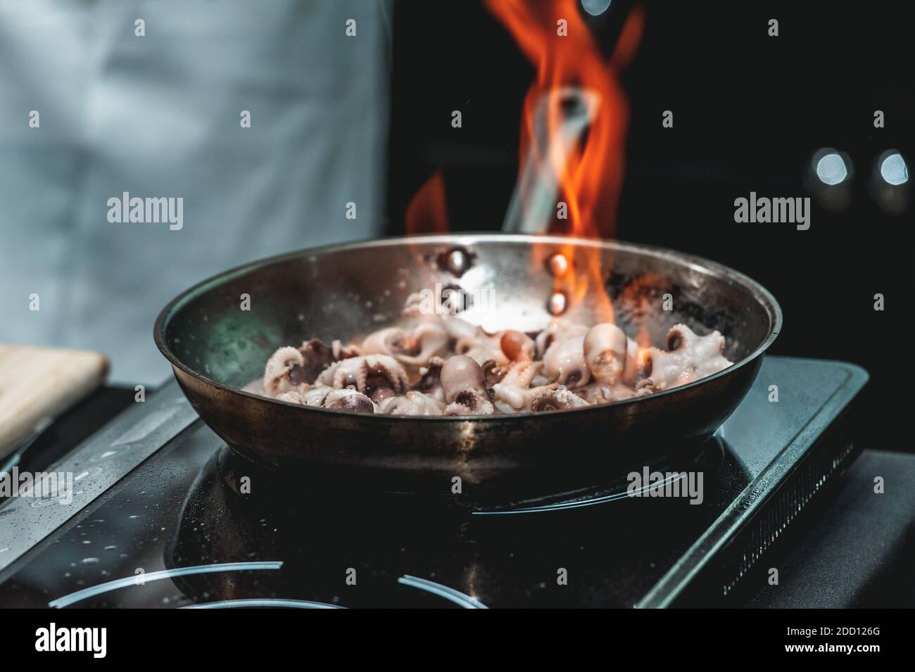 The chef cooks small octopus on a metal frying pan at the