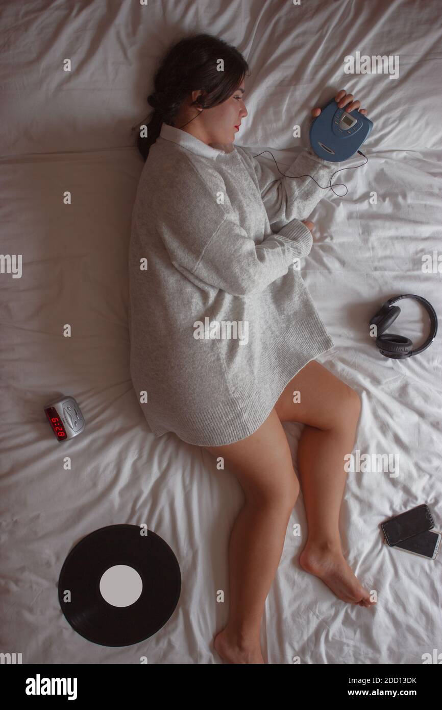 Brunette girl listening to music with a music player from the early 2000s lying on bed. Nostalgia concept. Winter Clothing 2020. Stock Photo