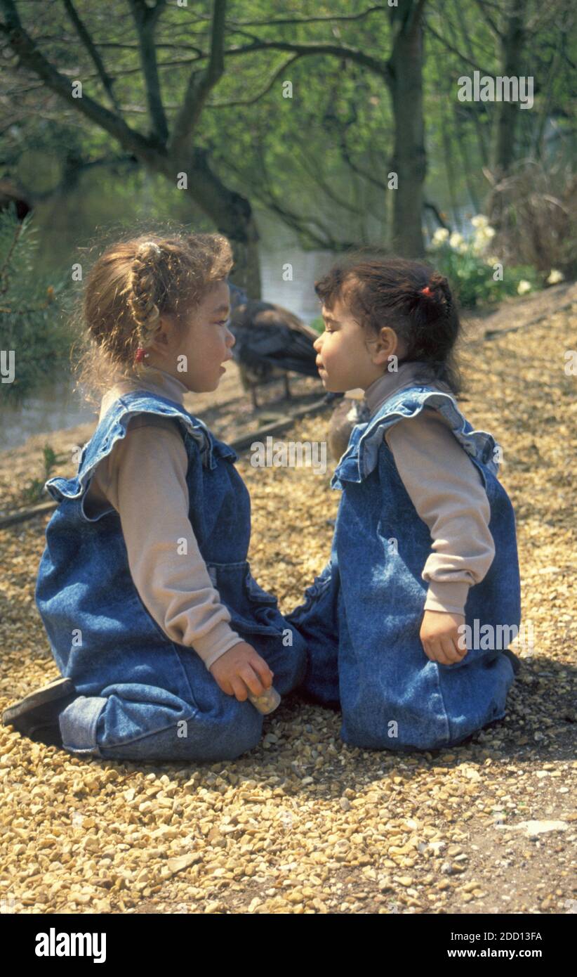 two little sister sitting by duck pond sitting face to face Stock Photo