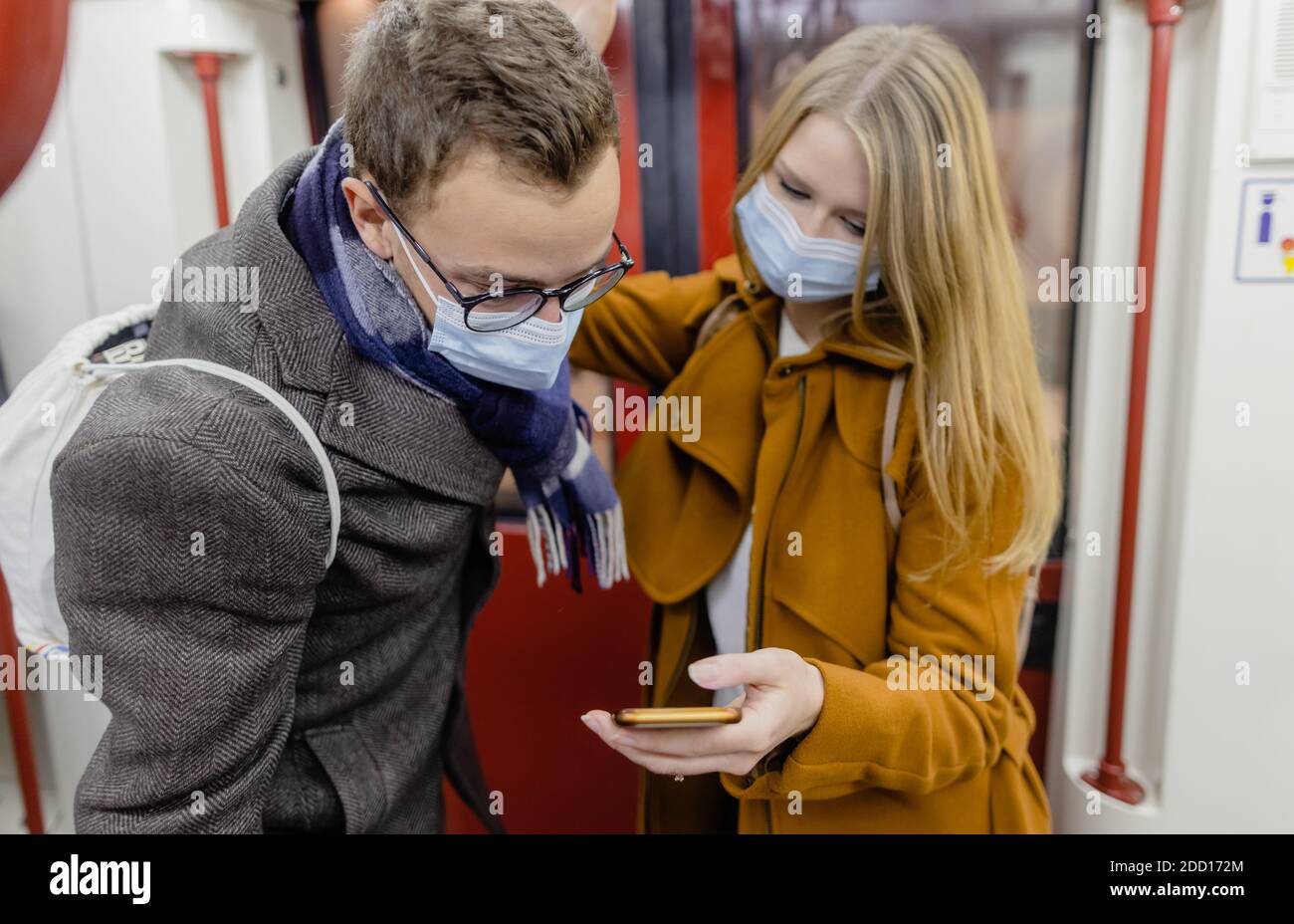 People using phone in train wearing covid-19 face mask Stock Photo