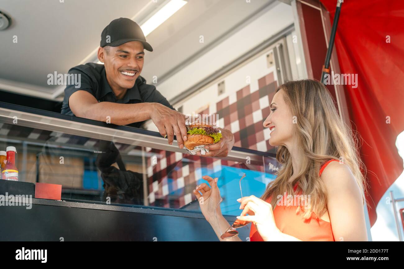 Cook in a food truck handing tasty burger over to woman customer Stock Photo