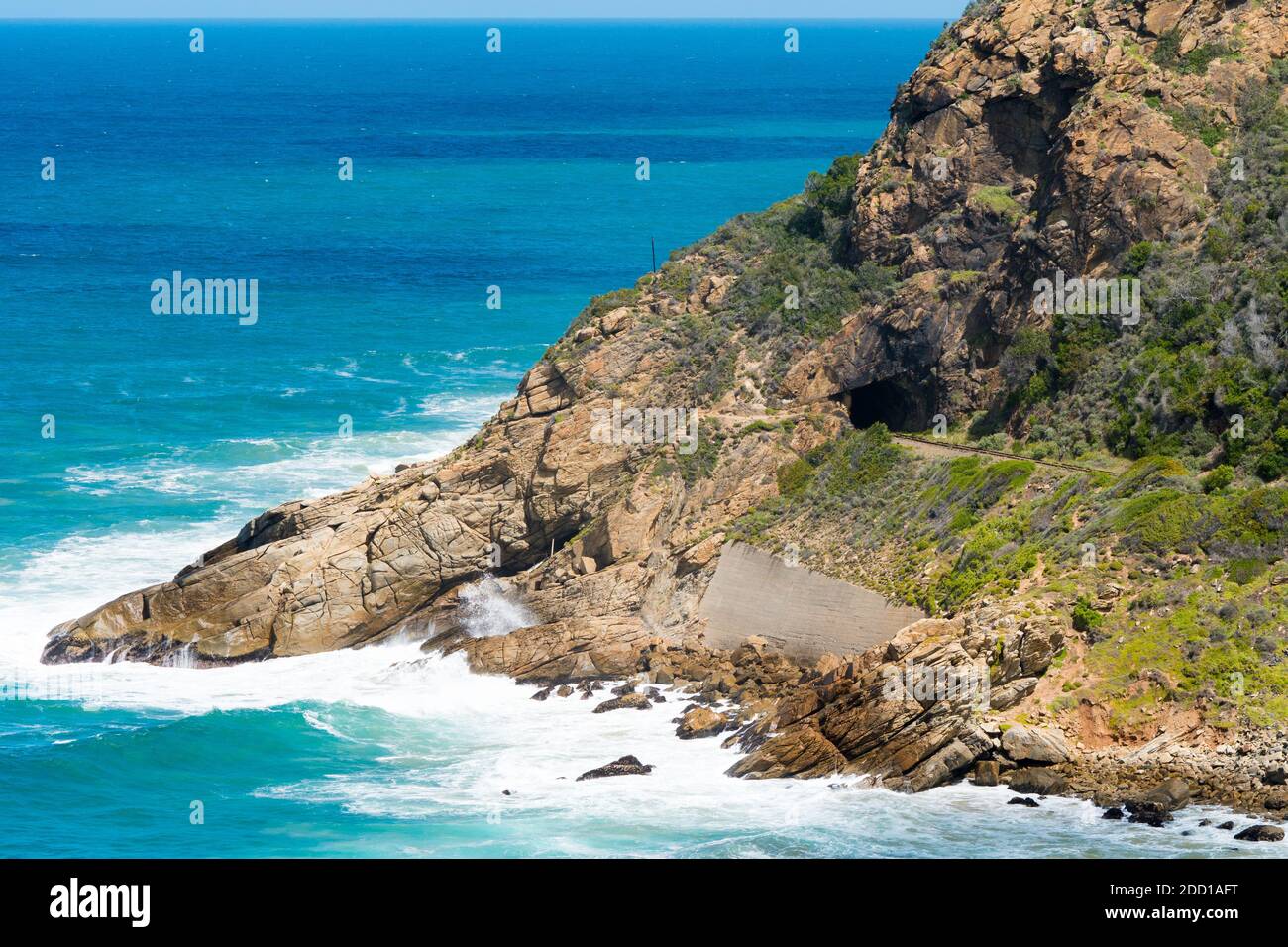 mountain cliff falling into the sea with a railway track and tunnel in the mountainside in Wilderness, Garden Route, South Africa Stock Photo