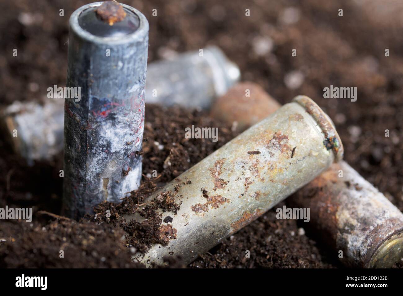 Corroded batteries covered with earth. Environmental protection and waste recycling. Closeup