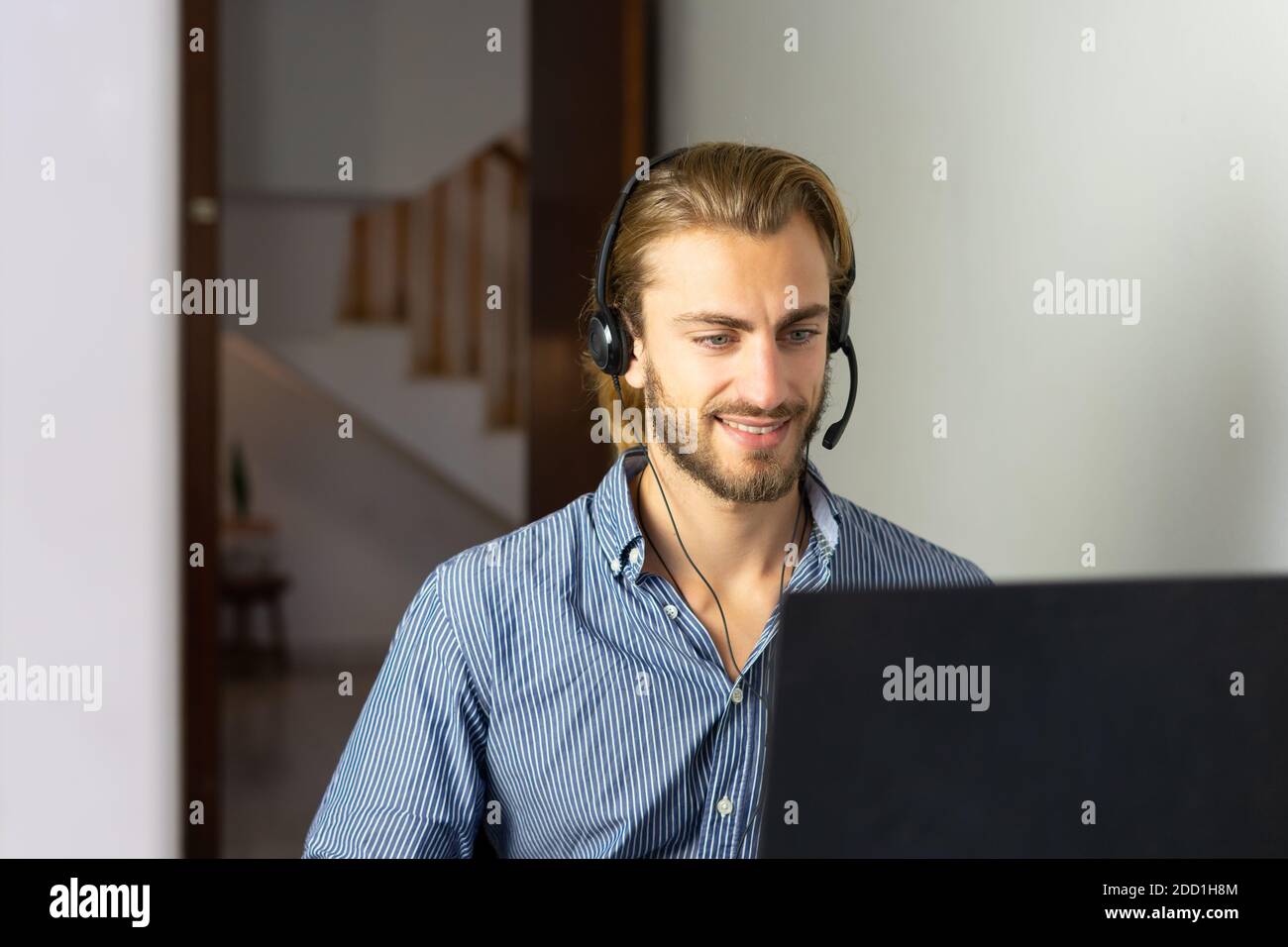 Blond male working from home with headphones using wireless internet on laptop, man call center agent or telemarketer Stock Photo
