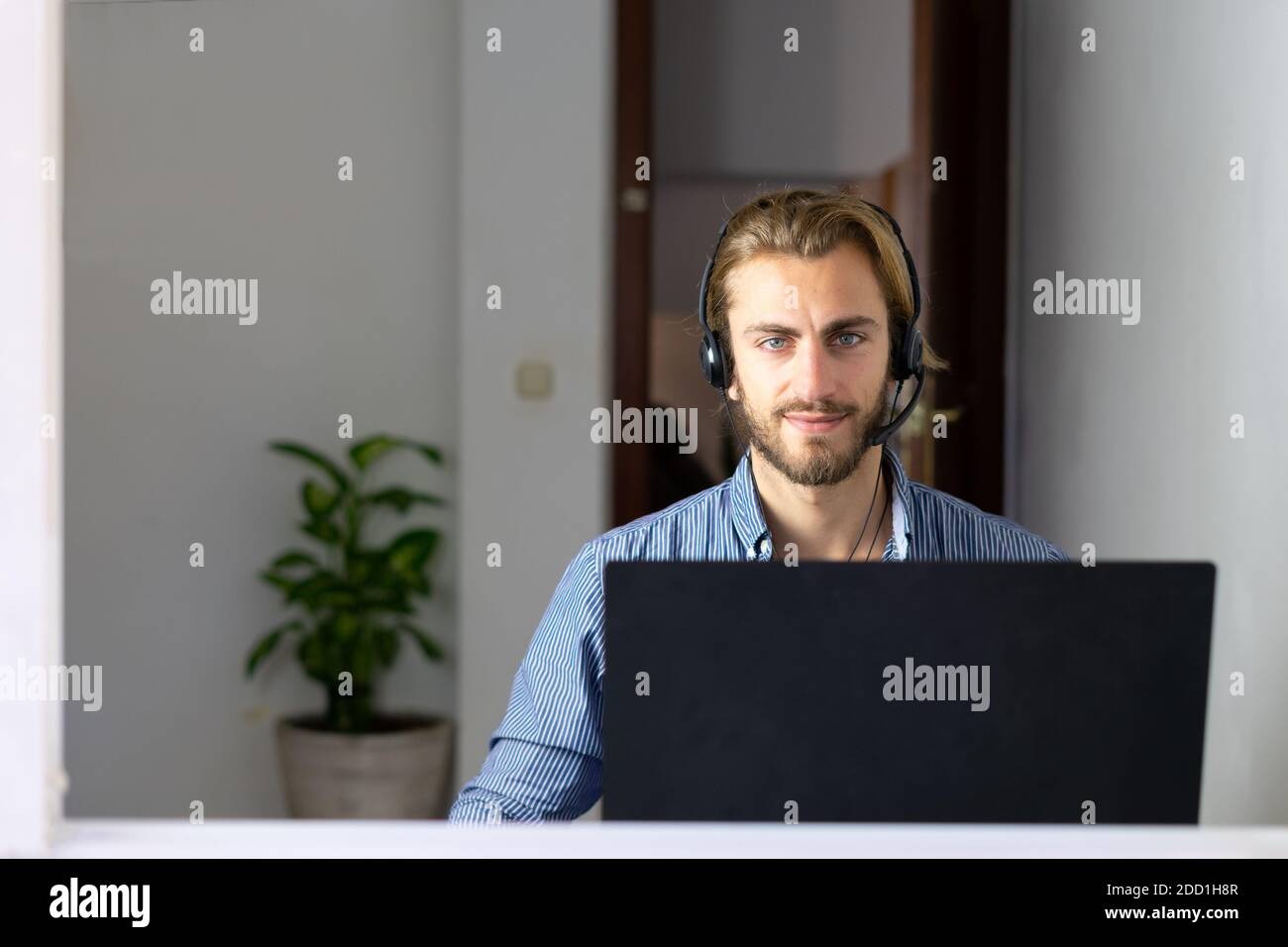 Blond male working from home with headphones using wireless internet on laptop, man call center agent or telemarketer Stock Photo