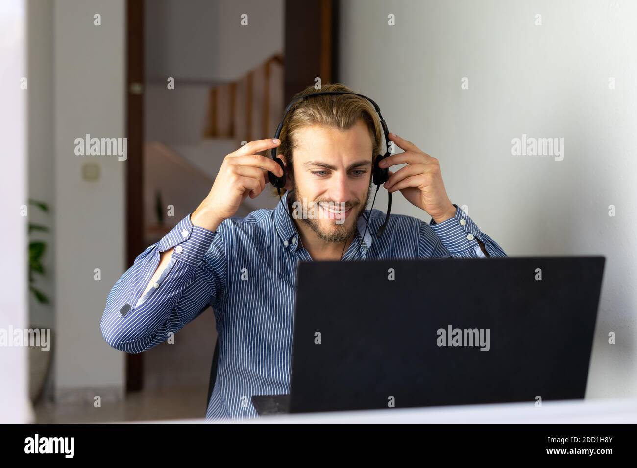 Blond male working from home with headphones using wireless internet on laptop, man call center agent or telemarketer Stock Photo