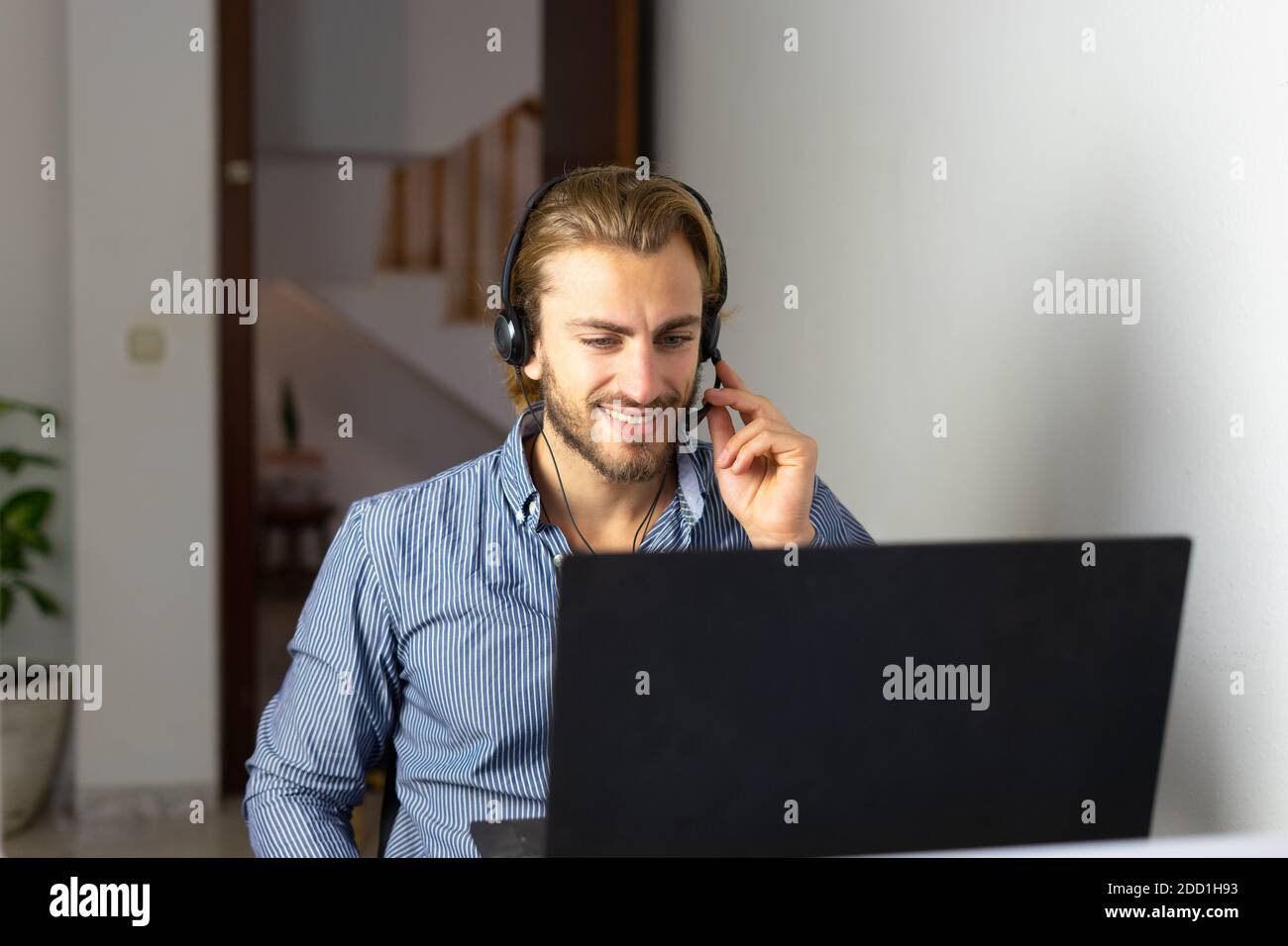 Blond male working from home with headphones using wireless internet on laptop, man call center agent or telemarketer Stock Photo