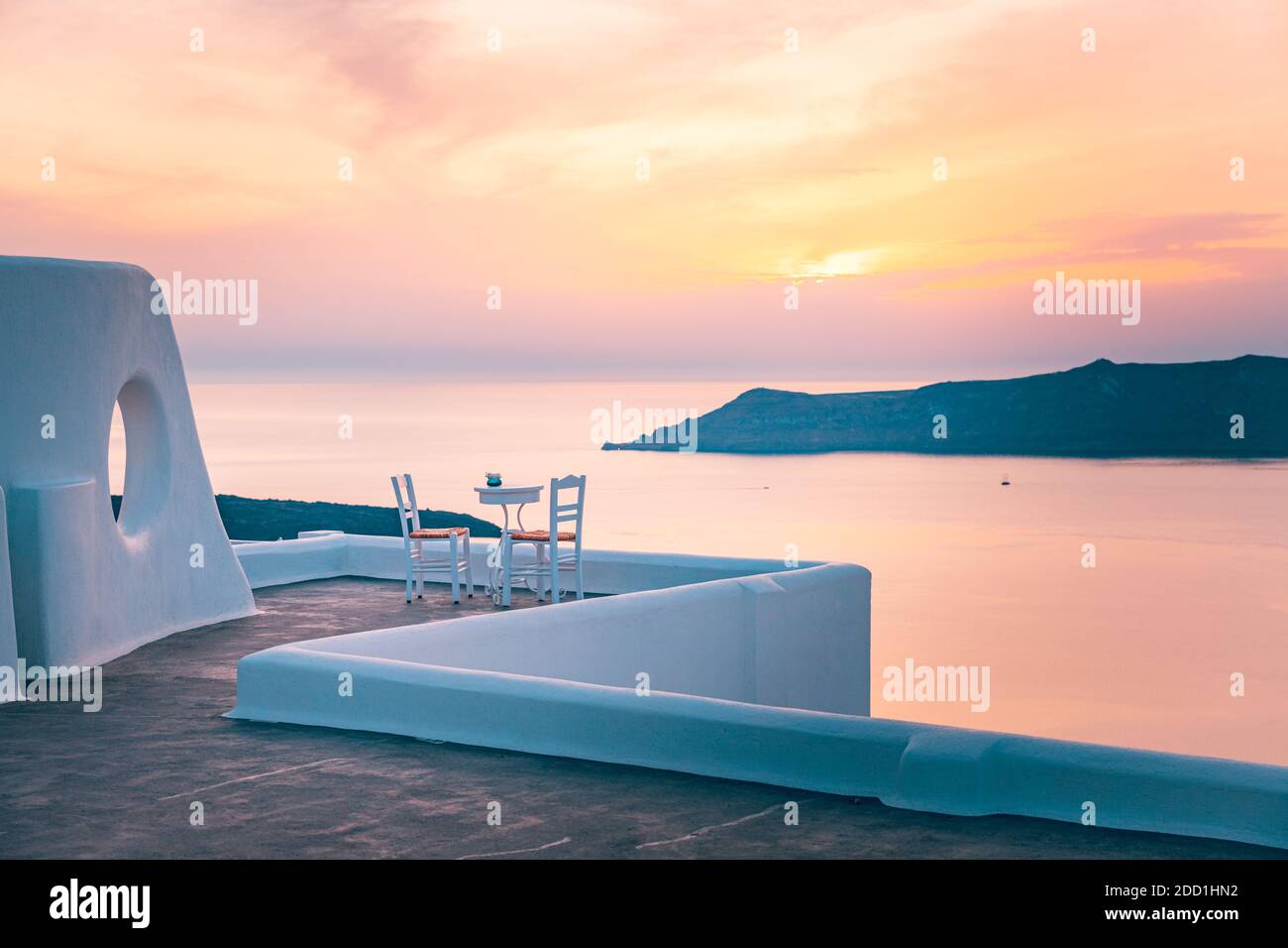 White architecture on Santorini island, Greece. Outdoor restaurant under a fantastic sunset landscape, chairs for couple. Romantic sunset view Stock Photo