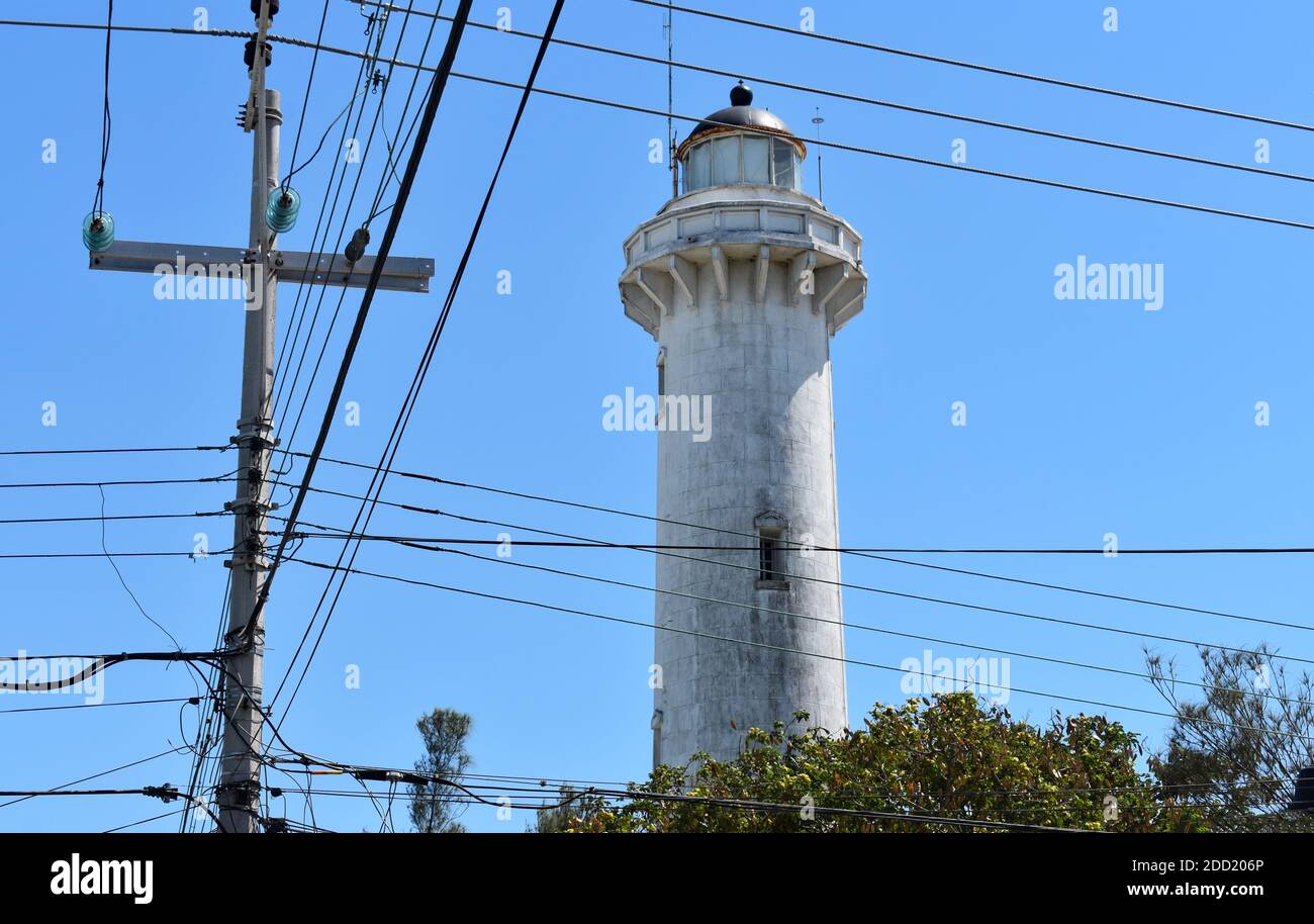 Faro de Progreso.  A white lighthouse in Progreso, Yucatan Peninsular, Mexico.  Telegraph pole with wires that cross the image and blue sky. Stock Photo