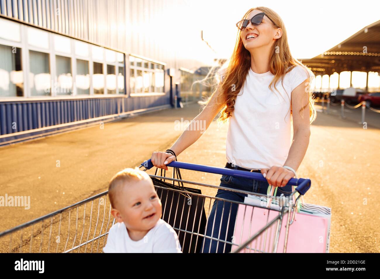 Happy young mother with baby and shopping bags and shopping trolley ...