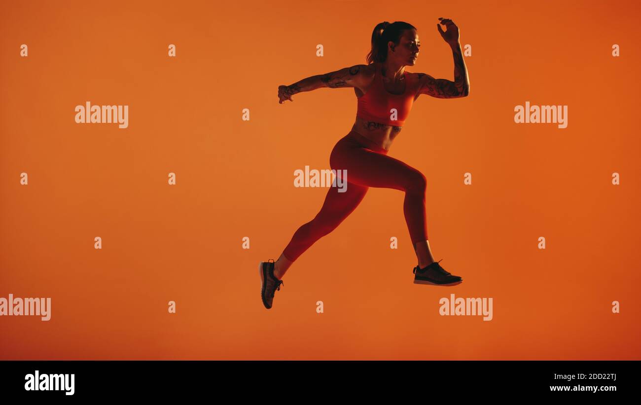 Female athlete running on orange background. Female sprinter taking stride forward while running. Stock Photo