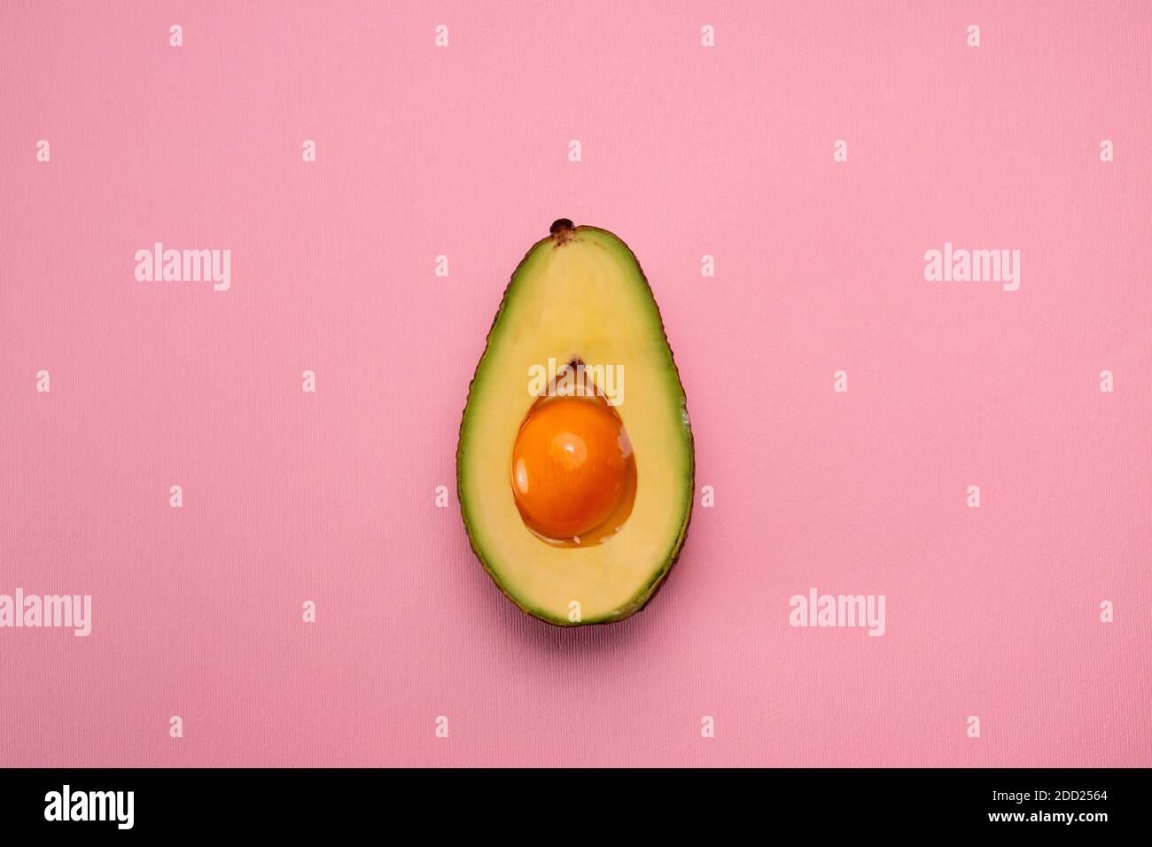 Avocado with egg yolk in middle on pink background. Creative food concept Stock Photo