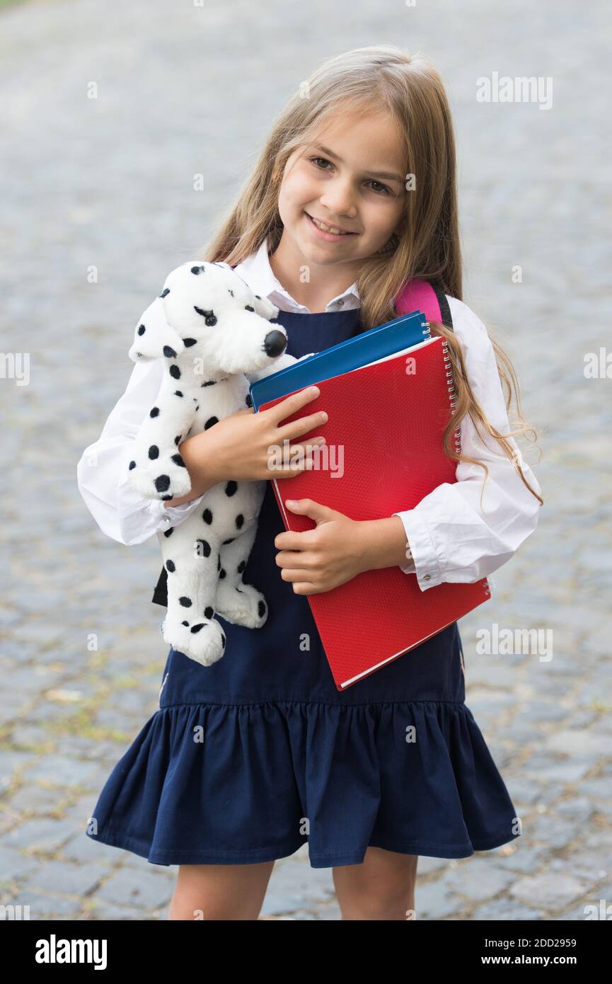 Adding fun to study. Happy child hold toy dog and books outdoors. Back to  school supplies. Fashion uniform. Formal dress code. Schoolwear. September  1. Primary education. Love your study more Stock Photo -