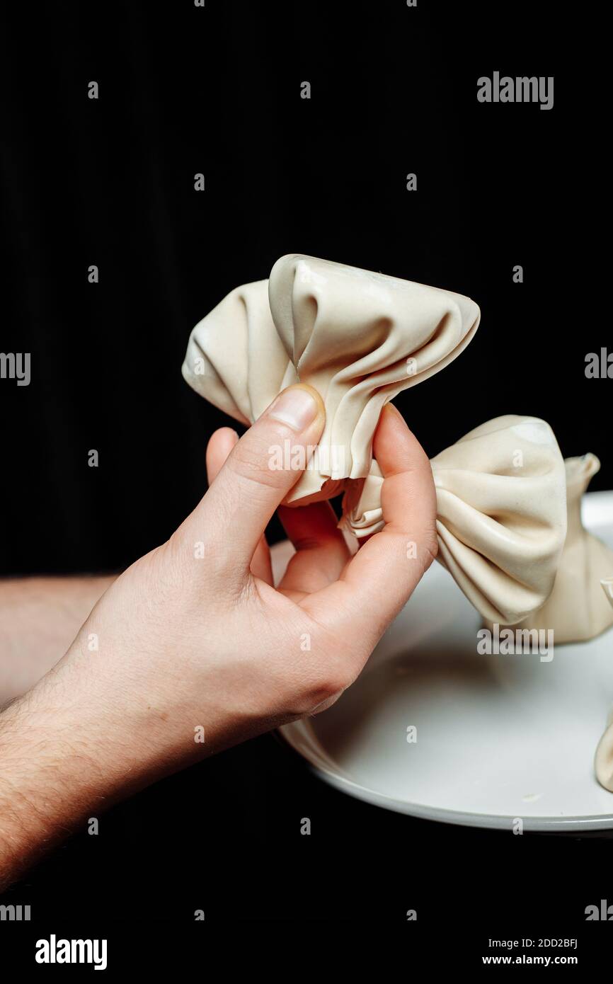 the hand holds the chikali by the tail. Khinkali in a Georgian restaurant in hand. Georgian cuisine Stock Photo