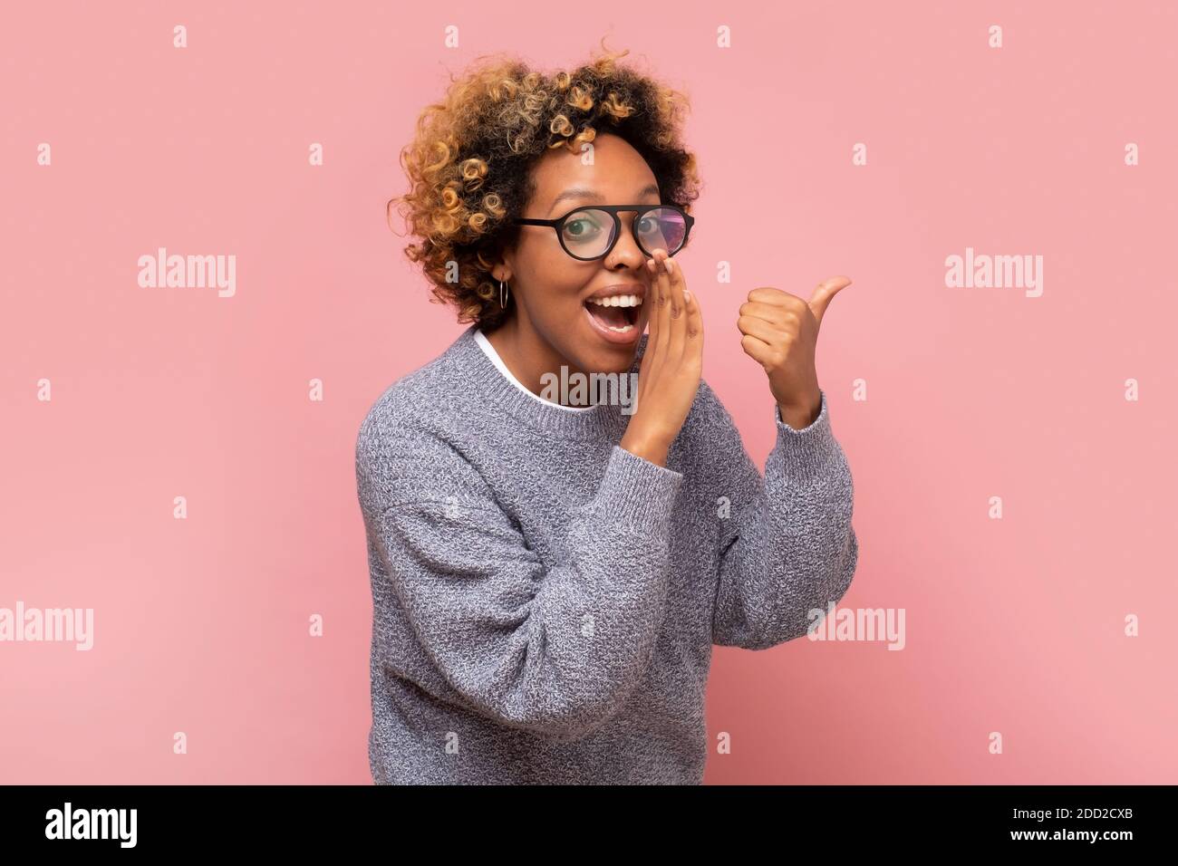 Young african american woman with hand on mouth telling secret or rumor, whispering. Studio shot on pink wall. Stock Photo