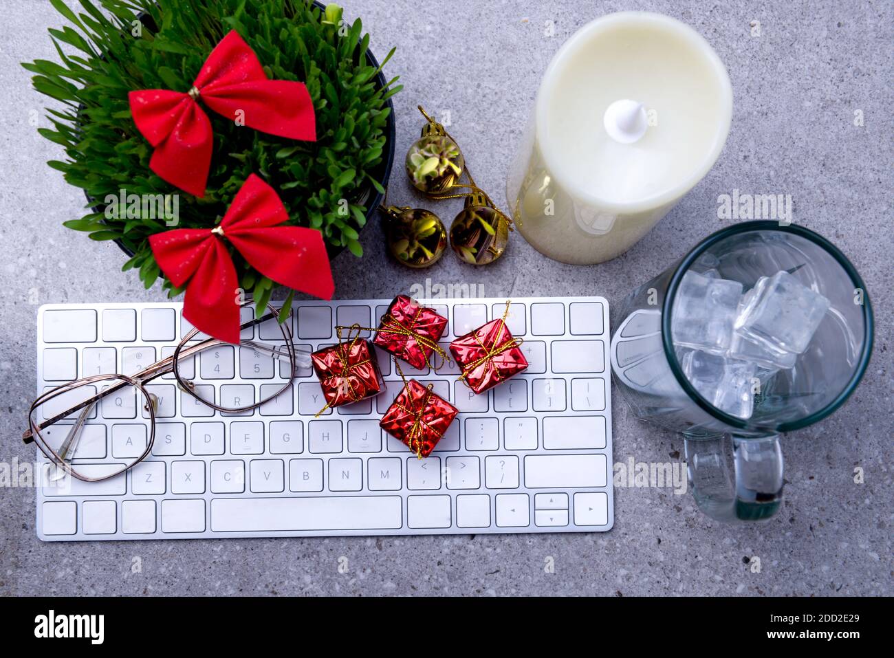 Close up view of millet grass plant in the pot with Christmas decoration, empty glass with an ice cube, and the keyboard on the desk Stock Photo