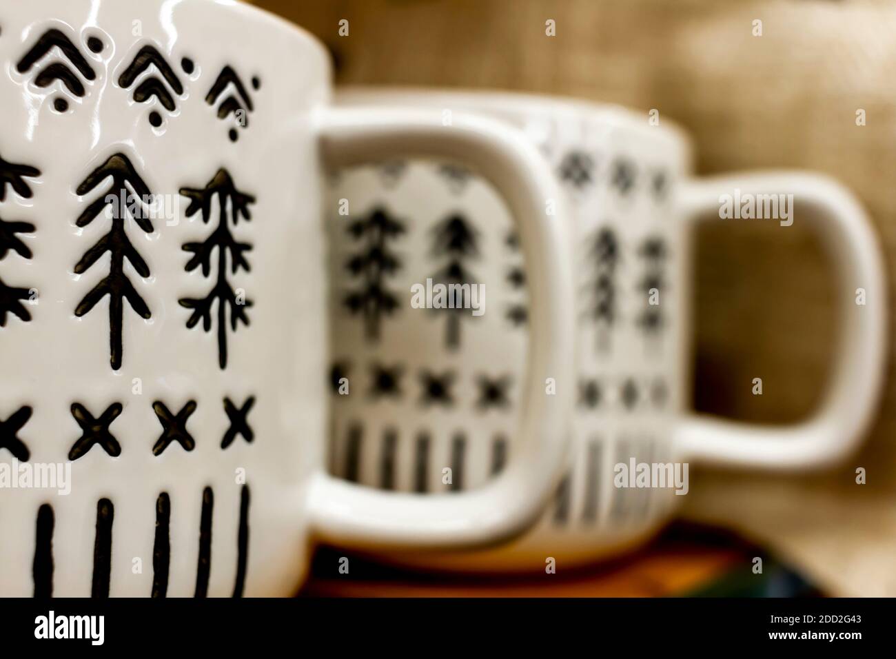 Two white porcelain coffee mugs with handles placed side by side on a shelf. They have black marks and textures in shapes of pine Christmas trees. A w Stock Photo