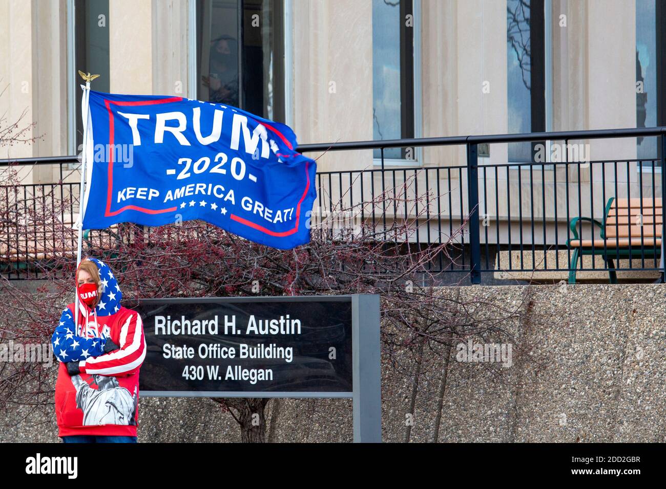 Lansing, Michigan, USA. 23rd Nov, 2020. A supporter of President Trump waves a flag outside the Michigan Secretary of State office as the Michigan Board of State Canvassers meets to decide whether to certify the results of the 2020 presidential election. The board subsequently certified the results, which showed Joe Biden ahead of President Trump by about 150,000 votes. Credit: Jim West/Alamy Live News Stock Photo