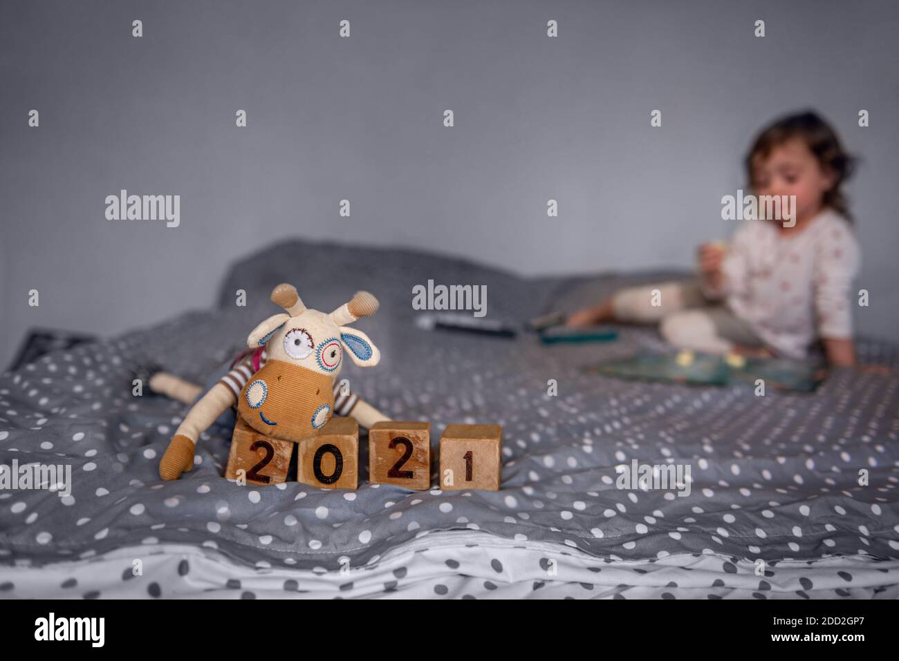 New Year's home card. Hand-made toy bull ox sits by wooden cubes with the numbers 2021. A child is playing on a blurr background, sitting on the couch Stock Photo