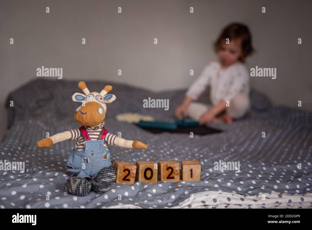 New Year's home card. Hand-made toy bull ox sits by wooden cubes with the numbers 2021. A child is playing on a blurr background, sitting on the couch Stock Photo
