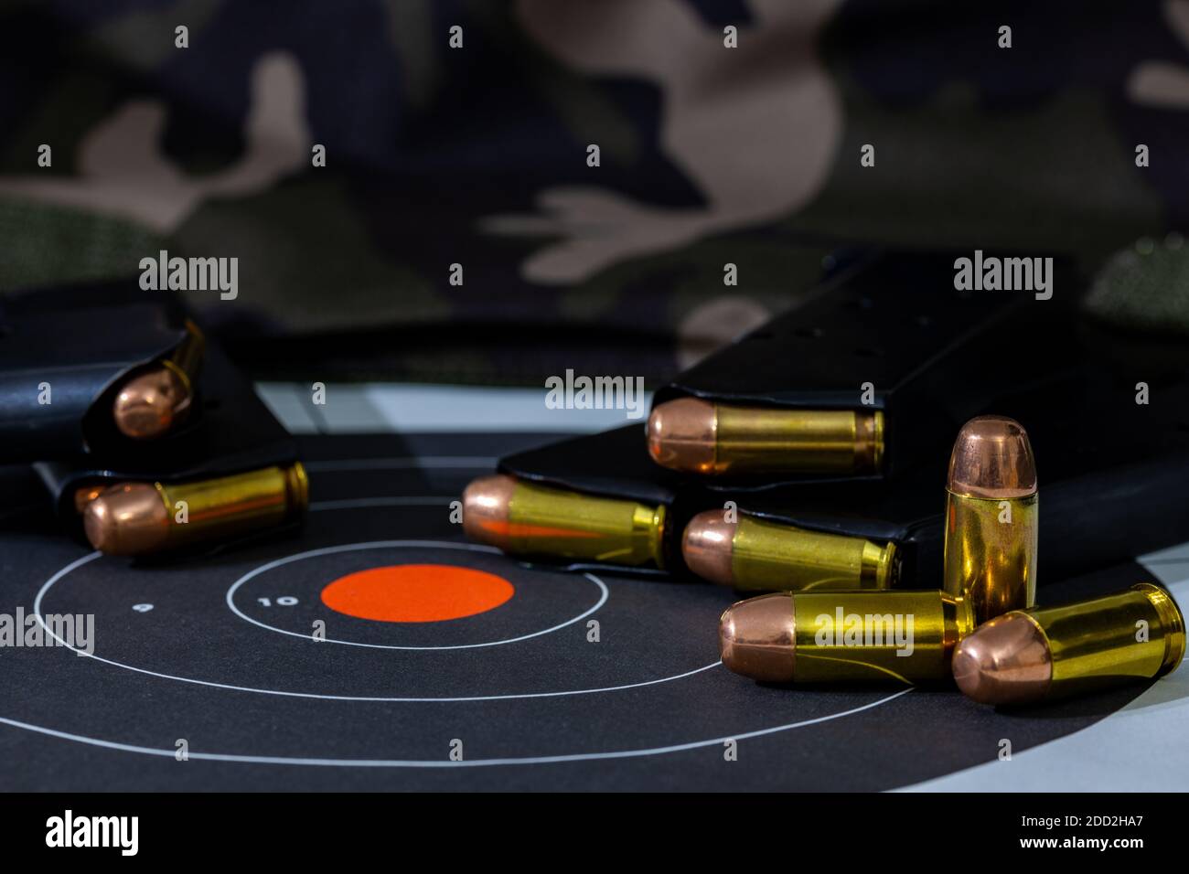 Loaded pistol magazines with loose rounds of ammunition scattered on top of a paper target with a camouflage background. Background and foreground blu Stock Photo