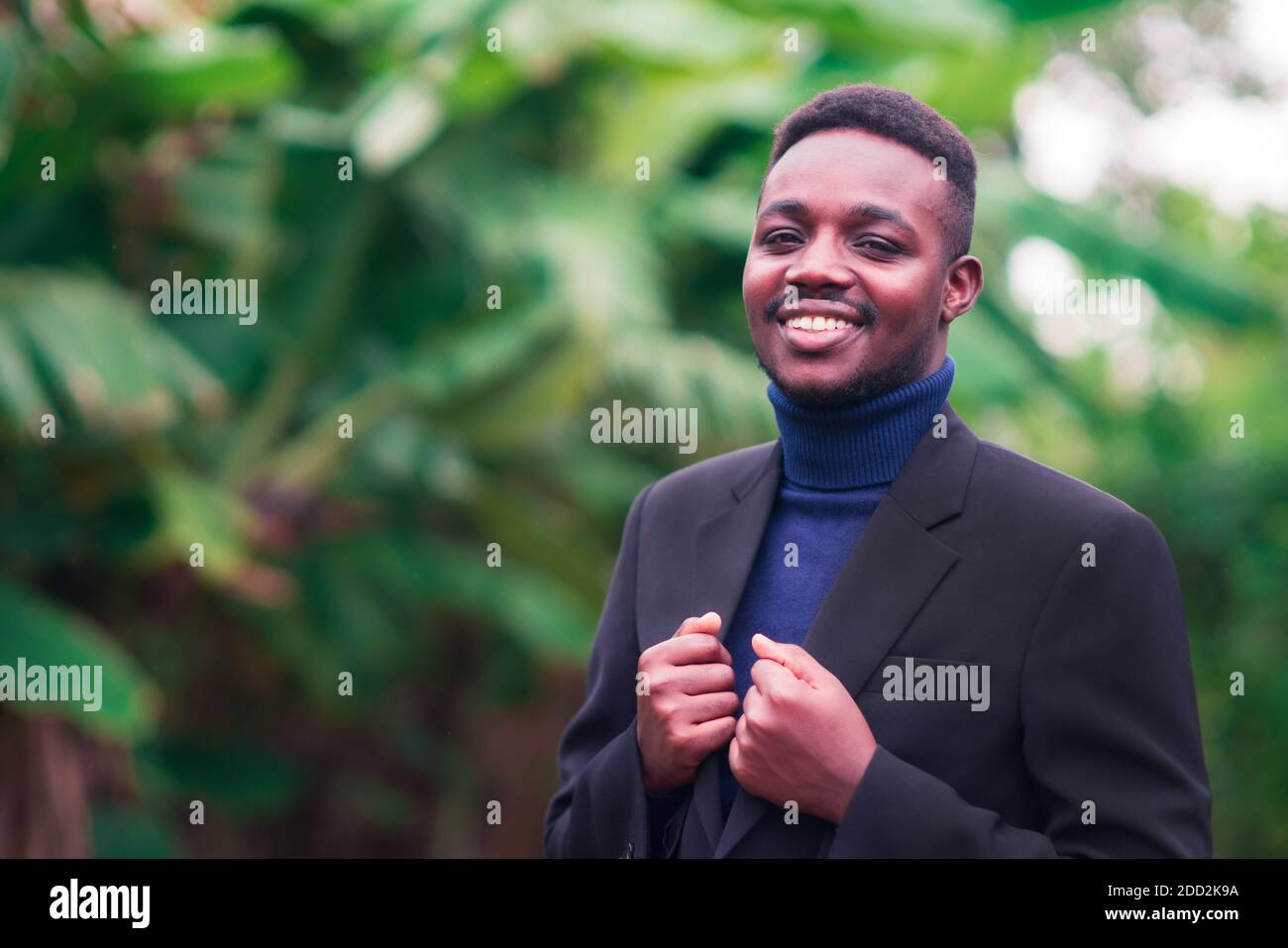Handsome african business man standing in trendy formal black suit. Guy with beard wearing blue long sleeve or sweater Stock Photo