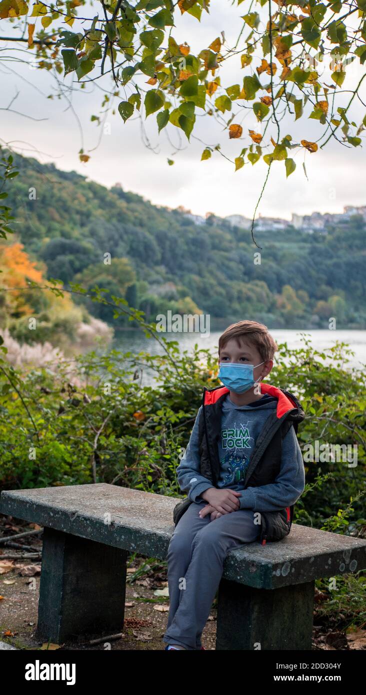 boy sitting on a bench in a medical mask, autumn park Stock Photo - Alamy