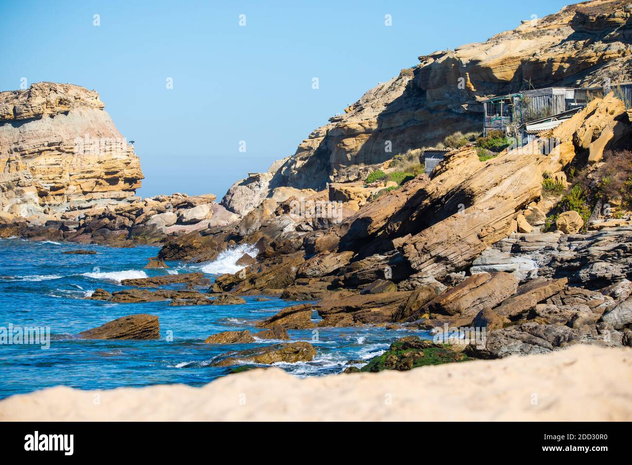 Stones and rocks on a beach under sky blue Atlantic Ocean against the cliffs during sunny day. Stock Photo