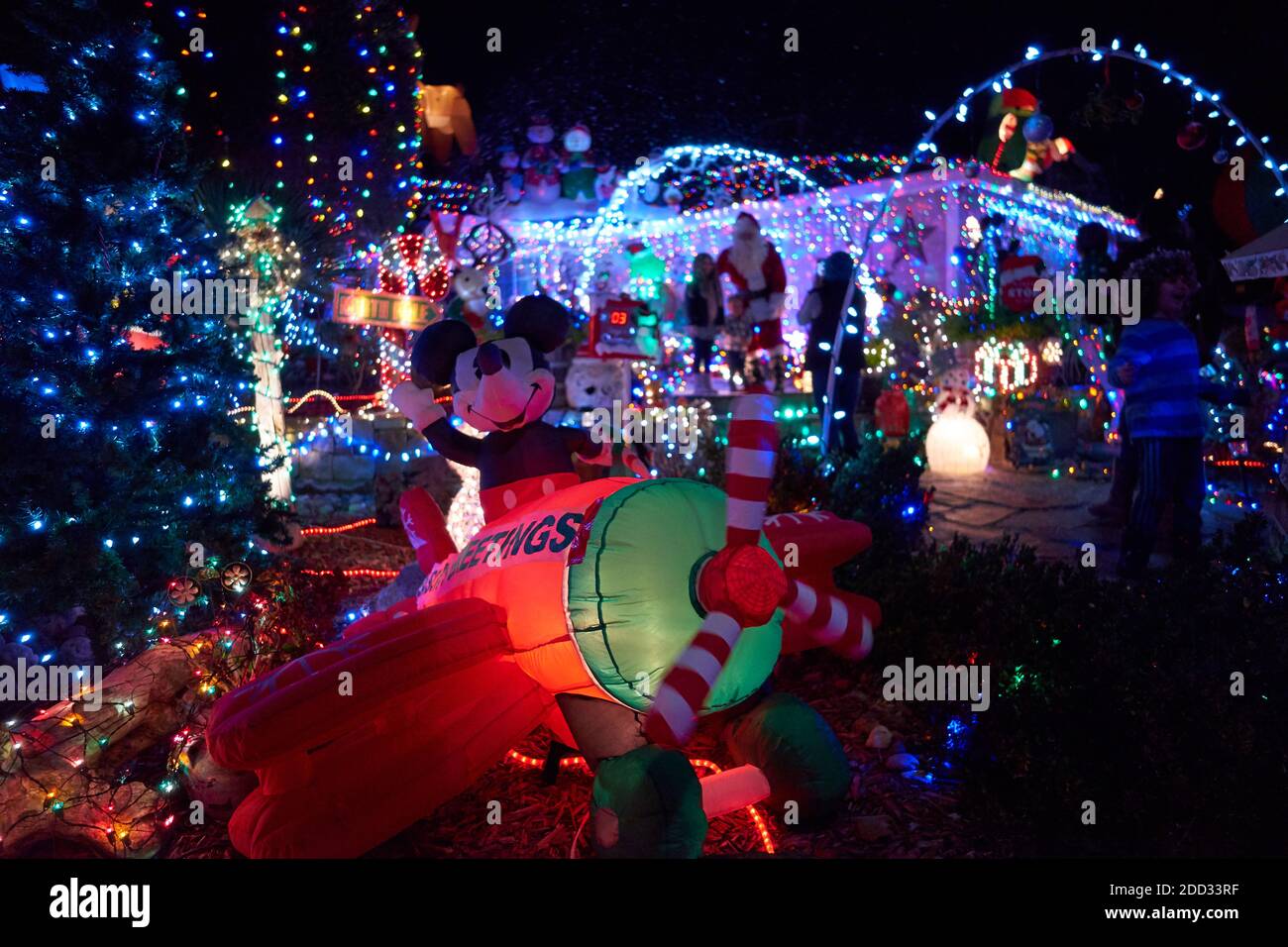 People visit a heavily decorated front lawn with bright colorful lights