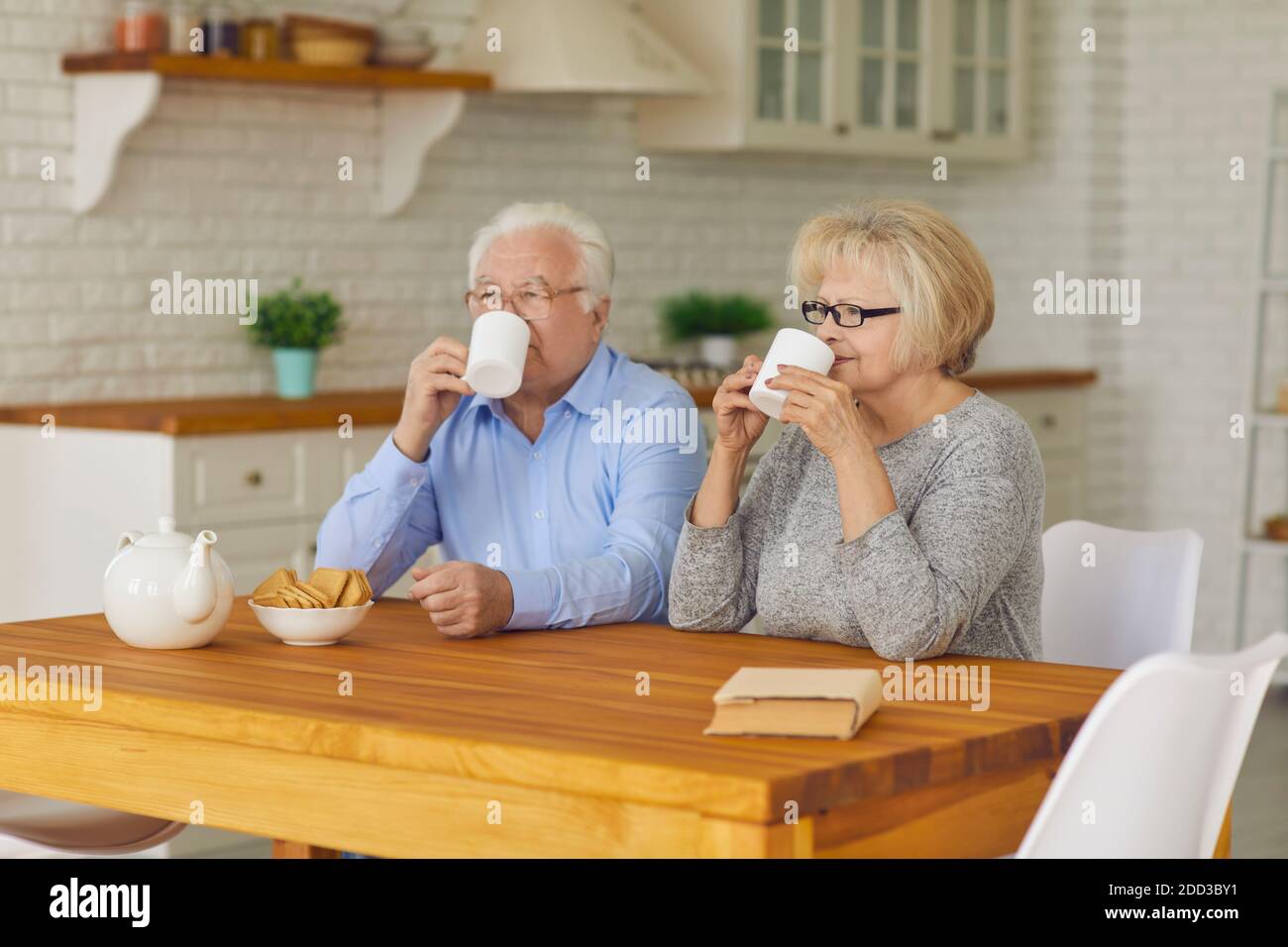 Senior couple with cups in their hands in the morning sitting in the kitchen drinking tea or coffee. Stock Photo