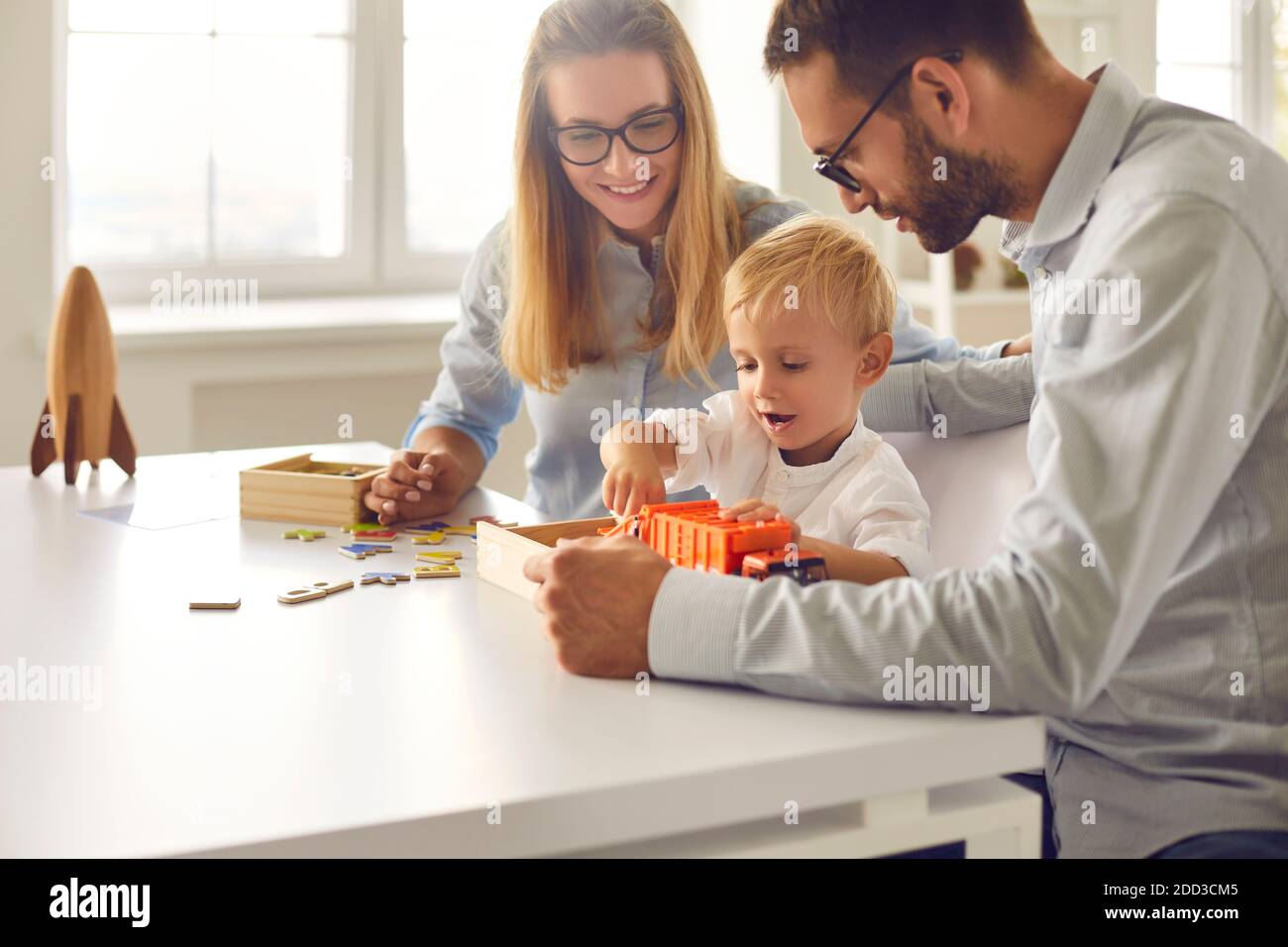 Mom, dad and their little son playing with toy truck together sitting at table at home Stock Photo