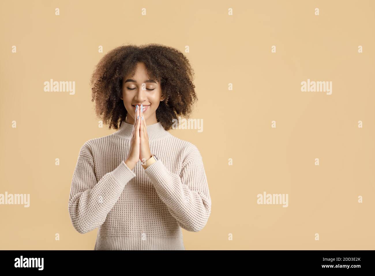 Calm smiling millennial female with closed eyes folded her hands in prayer Stock Photo