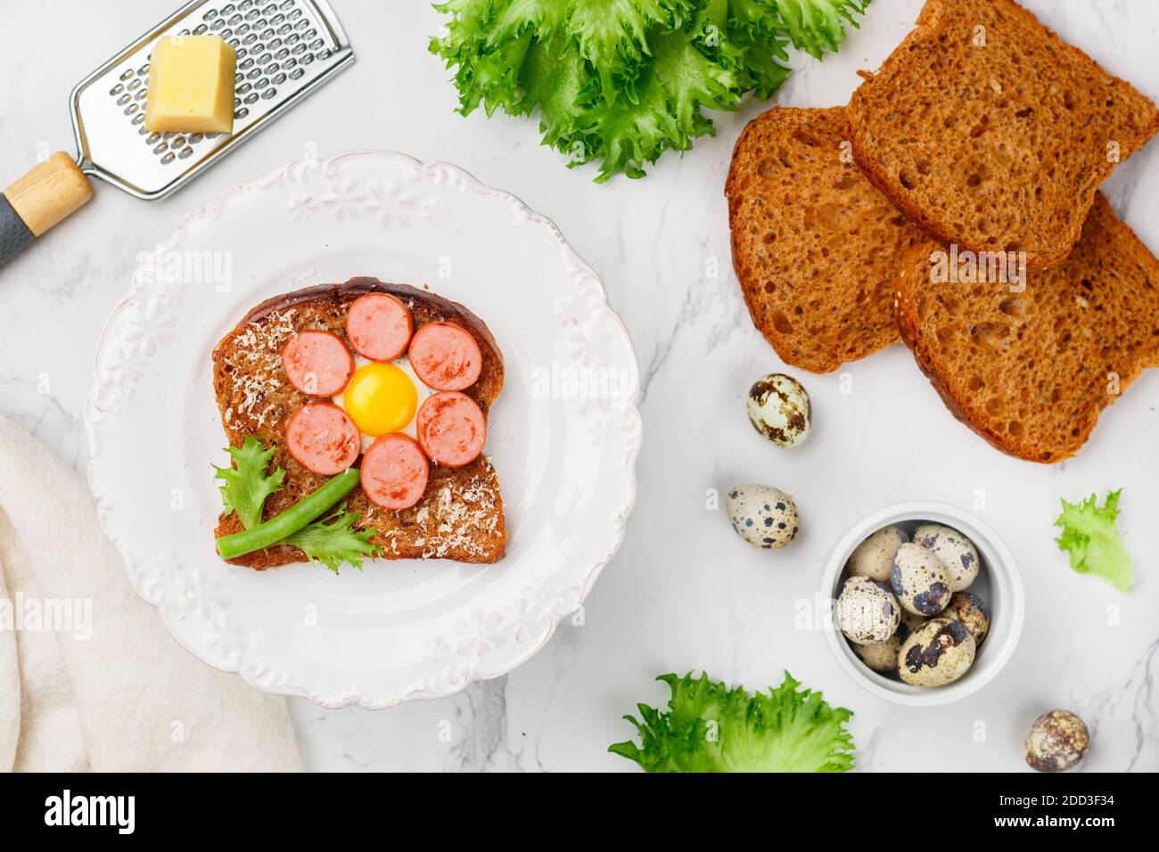 Delicious Breakfast of rye toast with cheese, sausage, quail egg, beans and lettuce. Children's sandwich. Selective focus Stock Photo