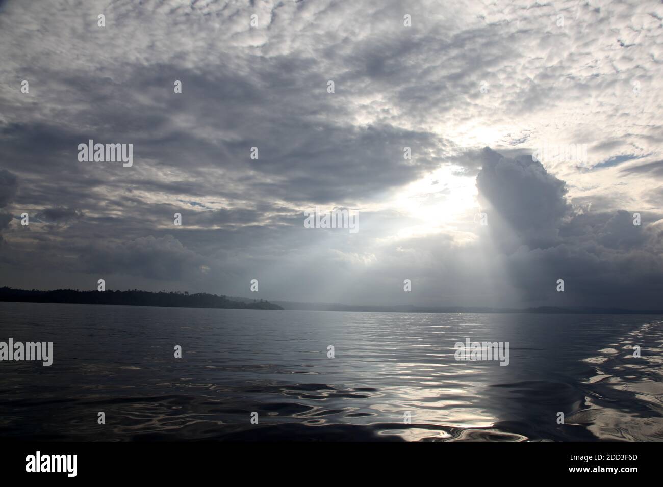 The sun peers through storm clouds on a still afternoon in the Mentawai Islands - Indonesia Stock Photo