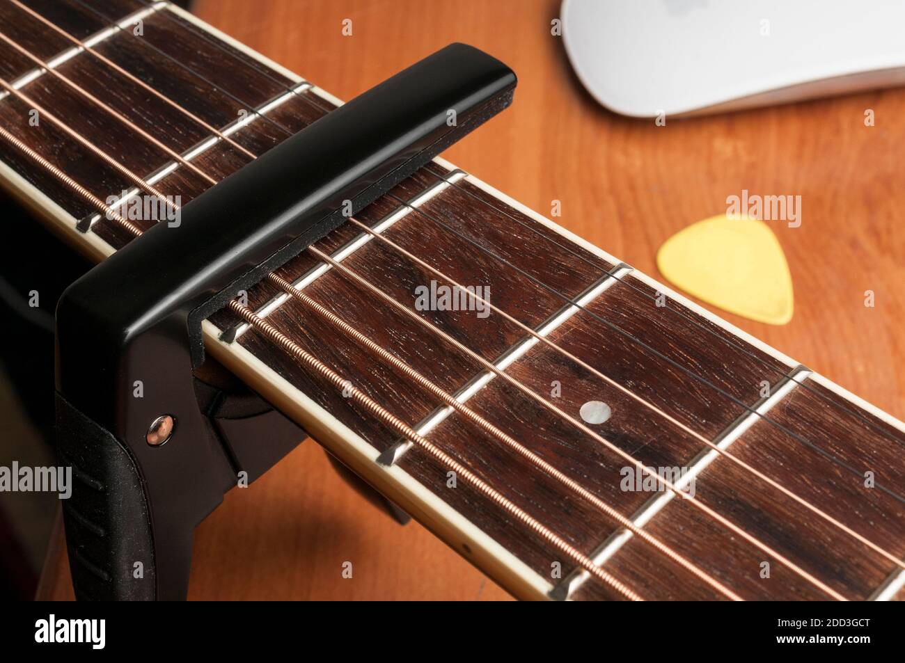 Acustic guitar with black metal capo on a wooden table Stock Photo - Alamy