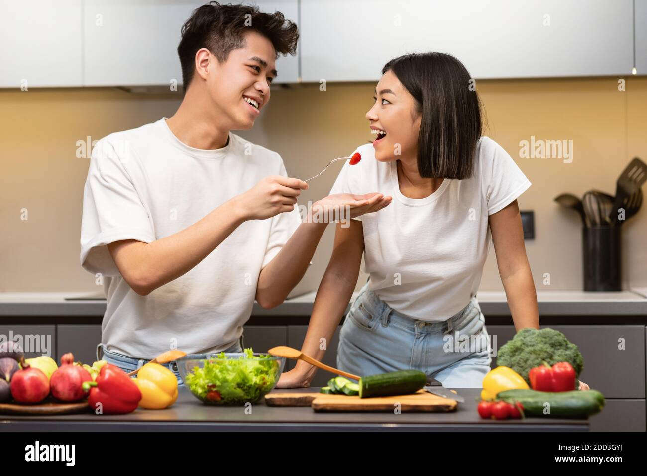 Korean Couple Cooking And Tasting Dinner Enjoying Meal In Kitchen Stock Photo