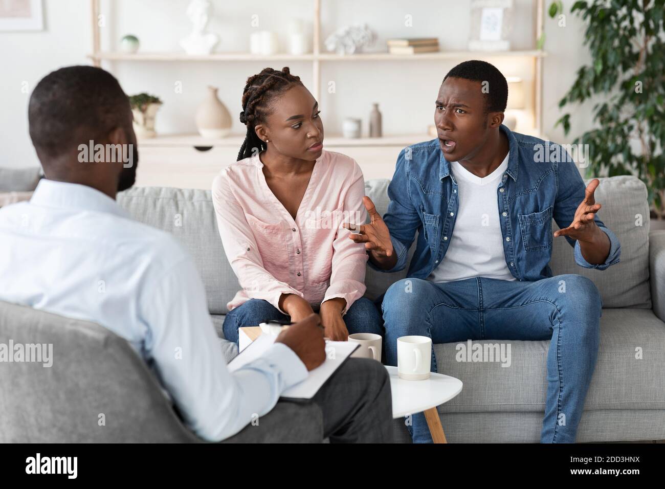 Young Black Spouses Having Relationship Problems, Sitting At Therapy Session With Counselor Stock Photo