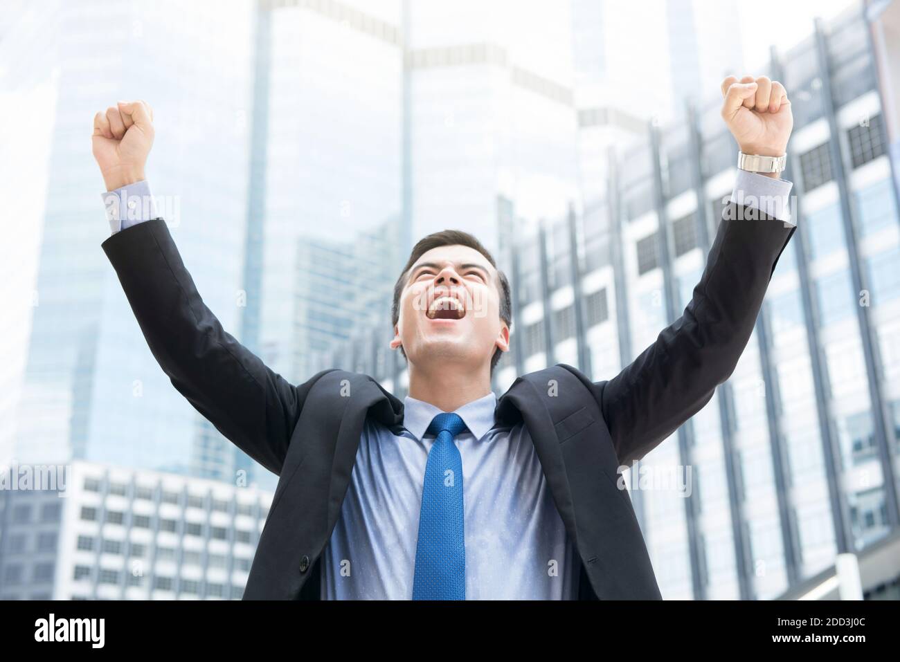 Businessman raising his fists in the air on blur office building ...