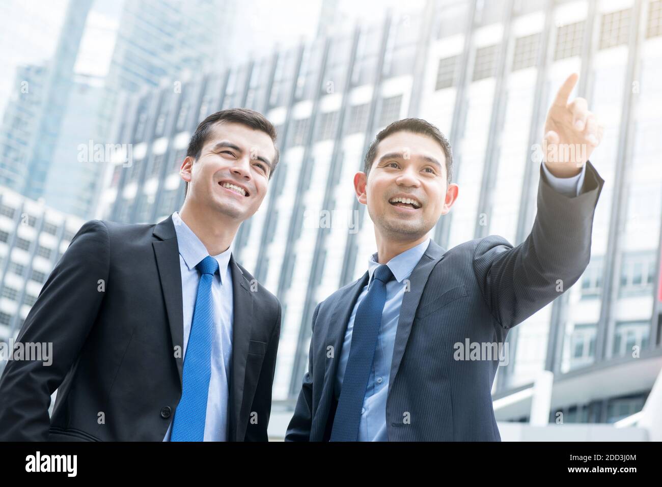 Two businessmen standing outdoors in the city with one hand pointing out - business partner and co-worker concepts Stock Photo