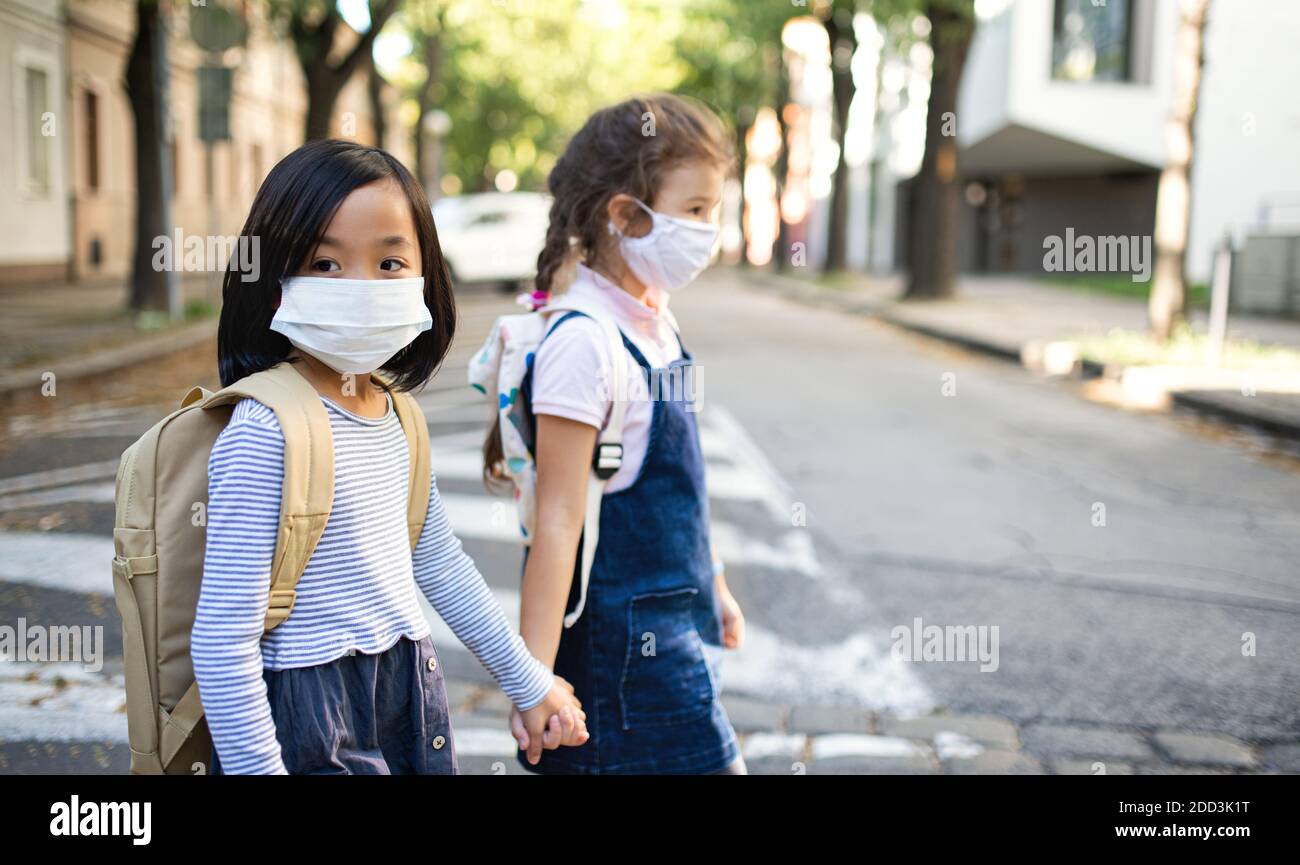 Small school girls with face mask outdoors in town, coronavirus concept. Stock Photo