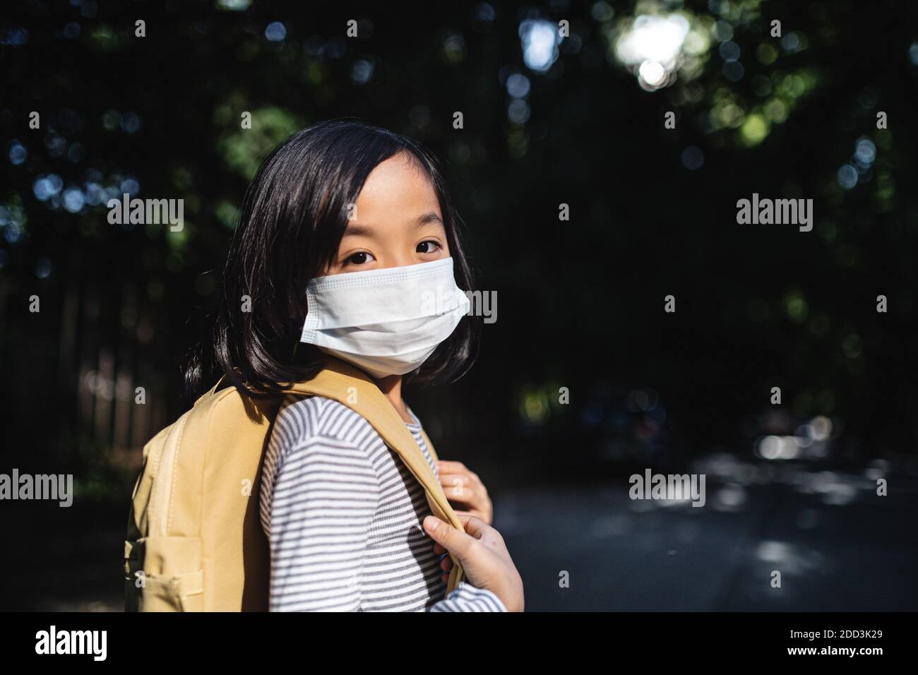 Portrait of small Japanese girl with backpack walking outdoors in town, coronavirus concept. Stock Photo