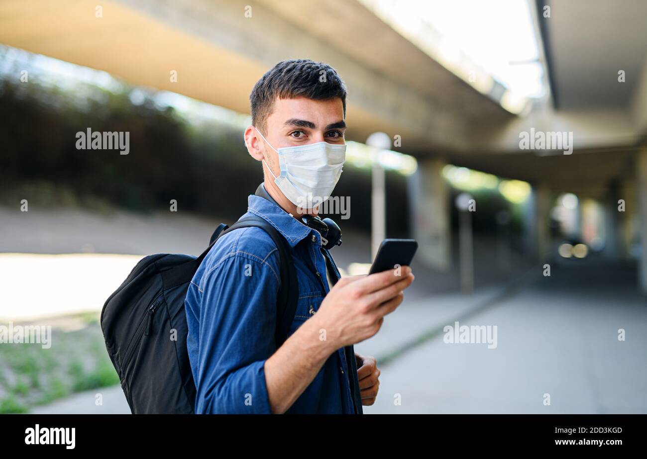 Portrait of young attractive man with smartphone walking outdoors in city, coronavirus concept. Stock Photo