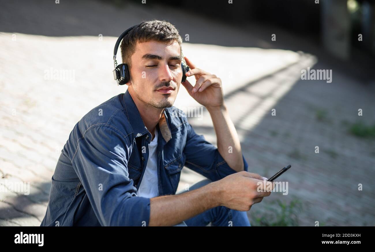 Portrait of young attractive man with smartphone sitting outdoors in city. Stock Photo