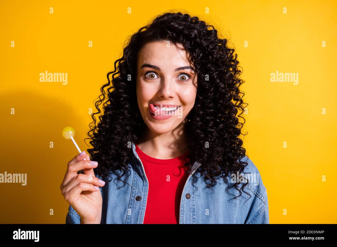 Photo of pretty lady hold lollipop stick out tongue lick lip wear red t-shirt jacket isolated yellow color background Stock Photo