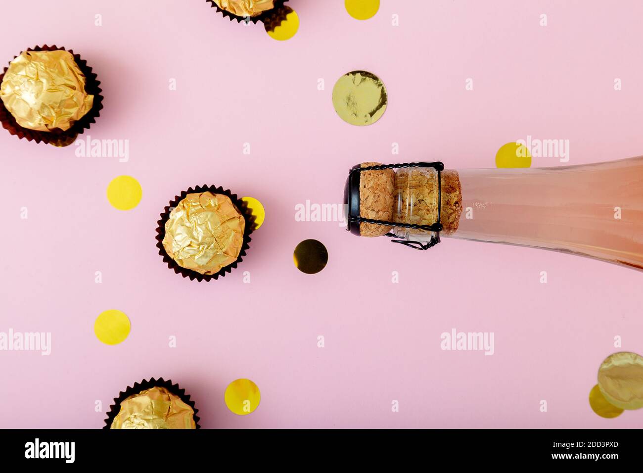 Bottle of pink champagne with confetti, golden candy on Pink background. Festive pastel gold celebration flat lay Stock Photo