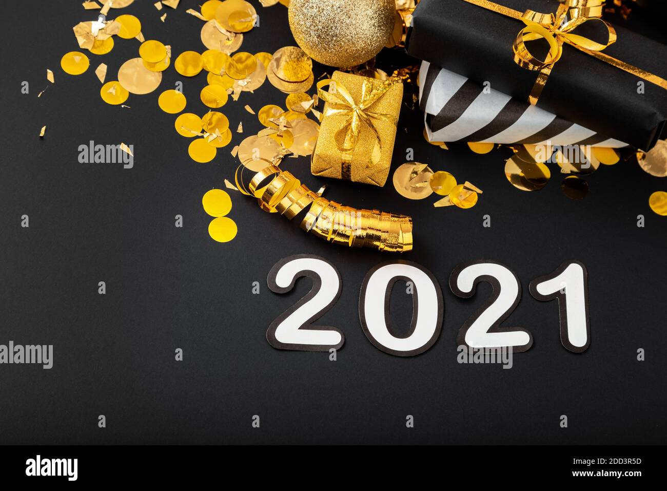 2021 white text lettering on black background with golden confetti, Christmas gift boxes gold balls festive decor. Happy New year event composition. Stock Photo