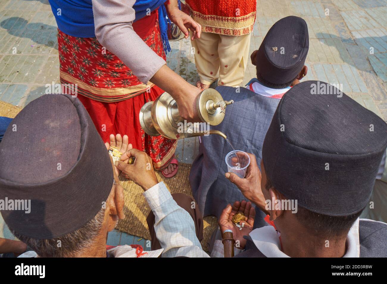 During a Nepalese festival. a woman dispenses drinking water to musicians accompanying a religious procession; Kathmandu, Nepal Stock Photo