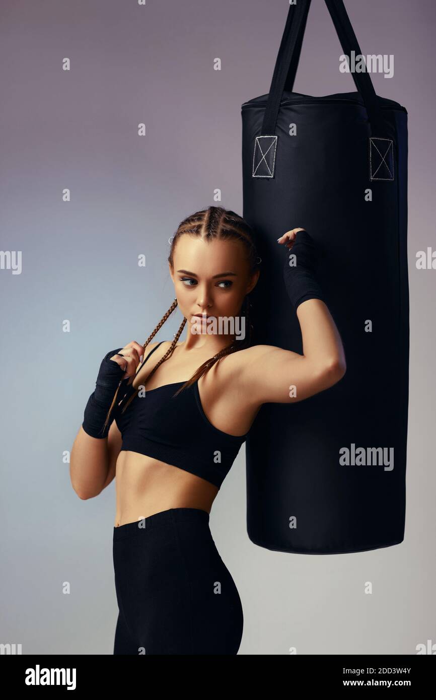 fit brunette woman in sportswear with boxing bandages near bag on gray background Stock Photo