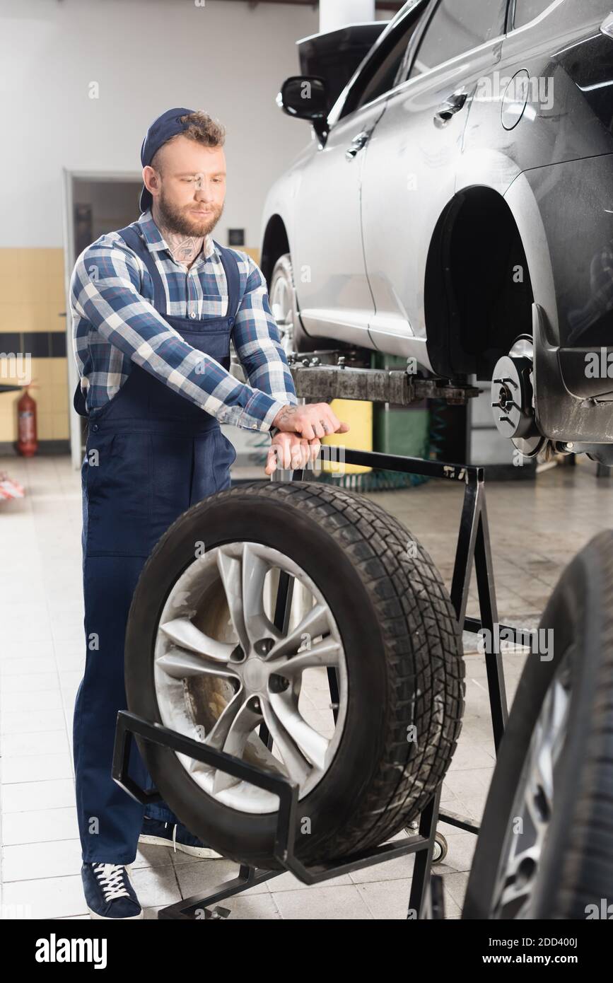 technician in workwear near wheel and automobile raised on car lift on